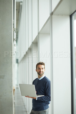Buy stock photo Cropped shot of a handsome young businessman standing indoors alone and using his laptop during the day