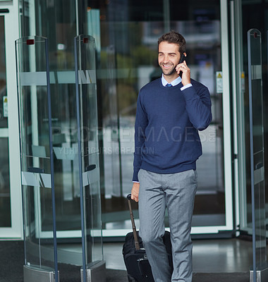 Buy stock photo Cropped shot of a handsome young businessman on the move with a suitcase while using his cellphone during the day