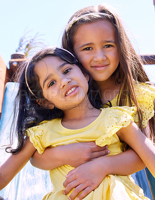 Buy stock photo Shot of a young girl embracing her younger sister while playing outside