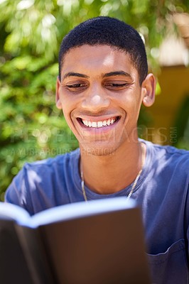 Buy stock photo Cropped shot of a handsome young man sitting alone outside and reading a book during the day