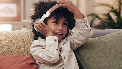 Buy stock photo Shot of an adorable little boy listening to music on headphones while sitting on a sofa at home