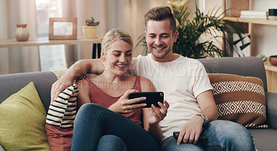 Buy stock photo Shot of a young couple using a smartphone on the sofa