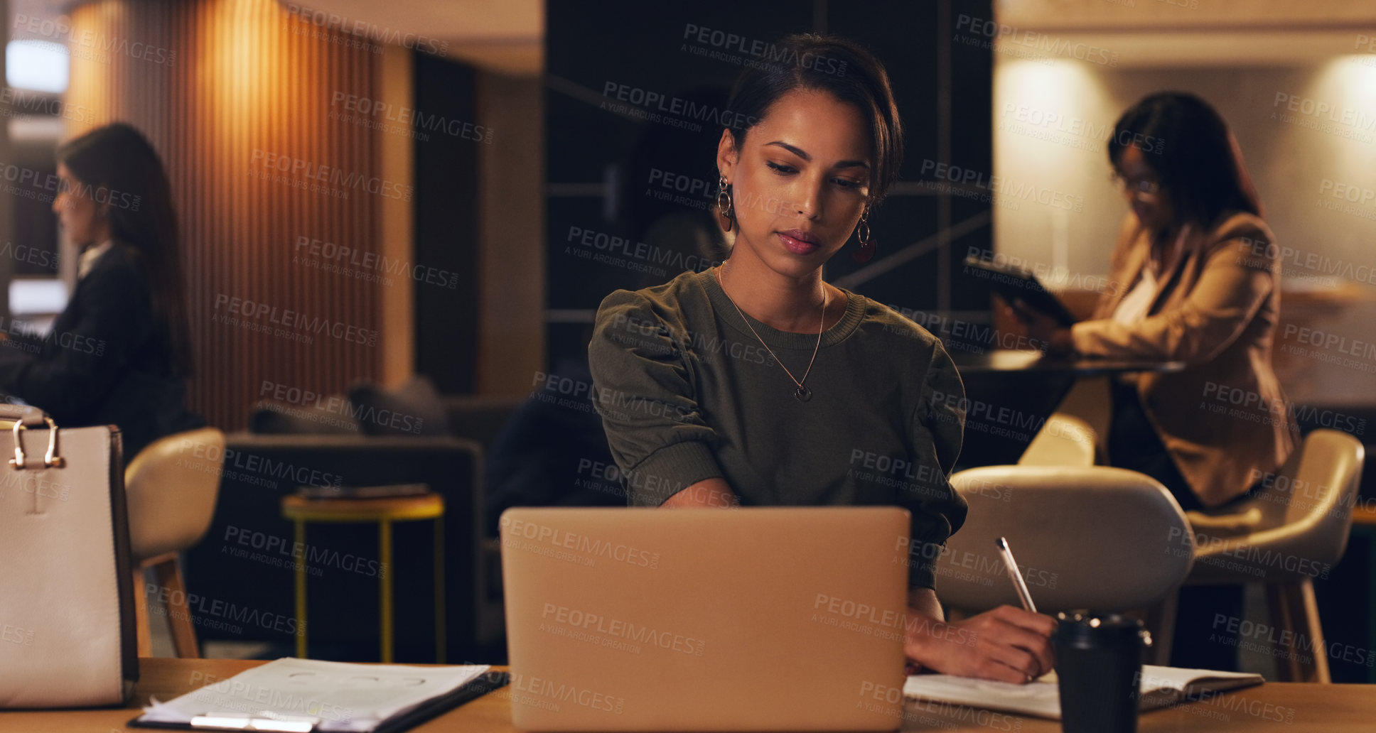 Buy stock photo Shot of a young businesswoman writing notes while working on a laptop in an office at night