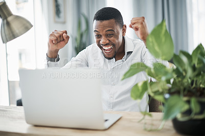 Buy stock photo Shot of a handsome young businessman sitting alone at home and celebrating while using his laptop