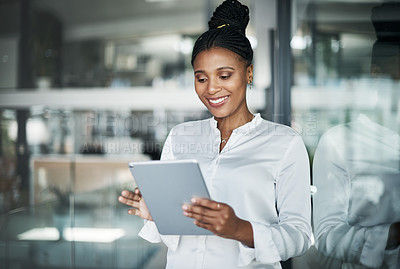 Buy stock photo Shot of an attractive young businesswoman standing alone in the office and using a digital tablet during the day