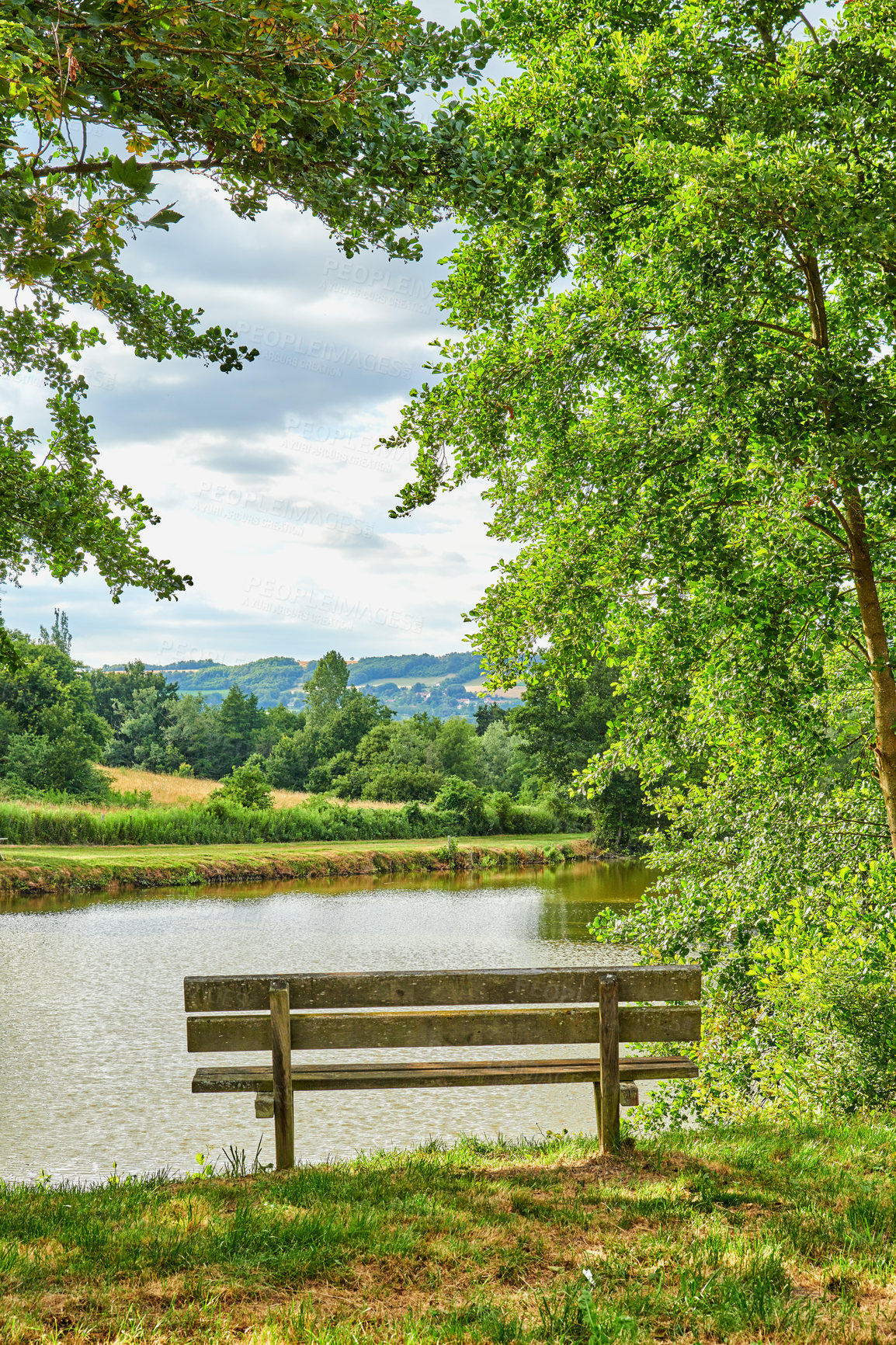 Buy stock photo A bench overlooking a lake in the countryside, surrounded by farmland and a forest close to Lyon, France. A quiet place to relax and reflect. Find some peace and tranquility outside in nature