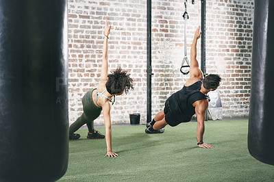 Buy stock photo Shot of two sporty young people doing the side plank at the gym