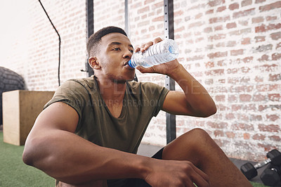 Buy stock photo Shot of a sporty young man drinking a bottle of water at the gym