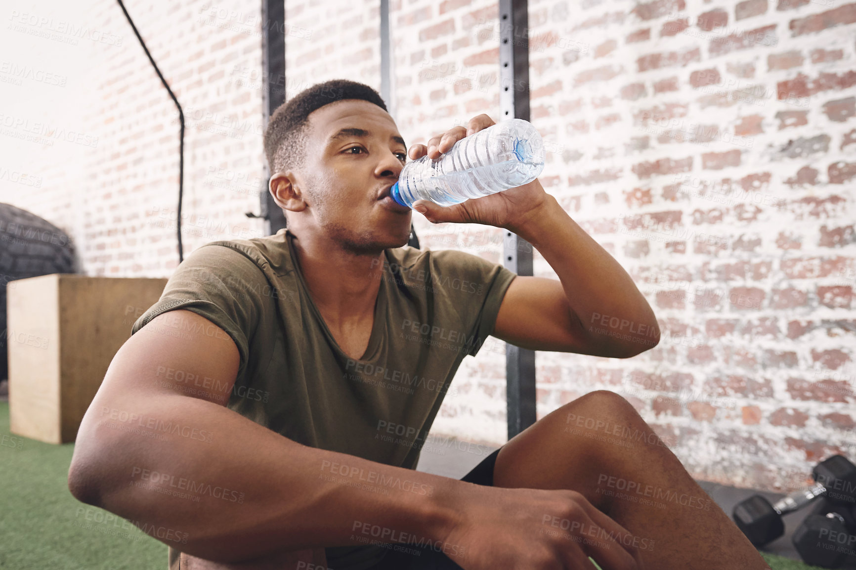 Buy stock photo Shot of a sporty young man drinking a bottle of water at the gym