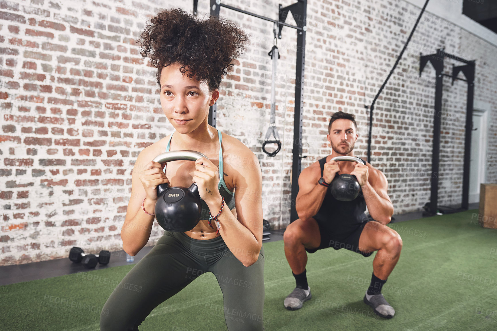 Buy stock photo Shot of two sporty young people using kettlebells while working out at the gym