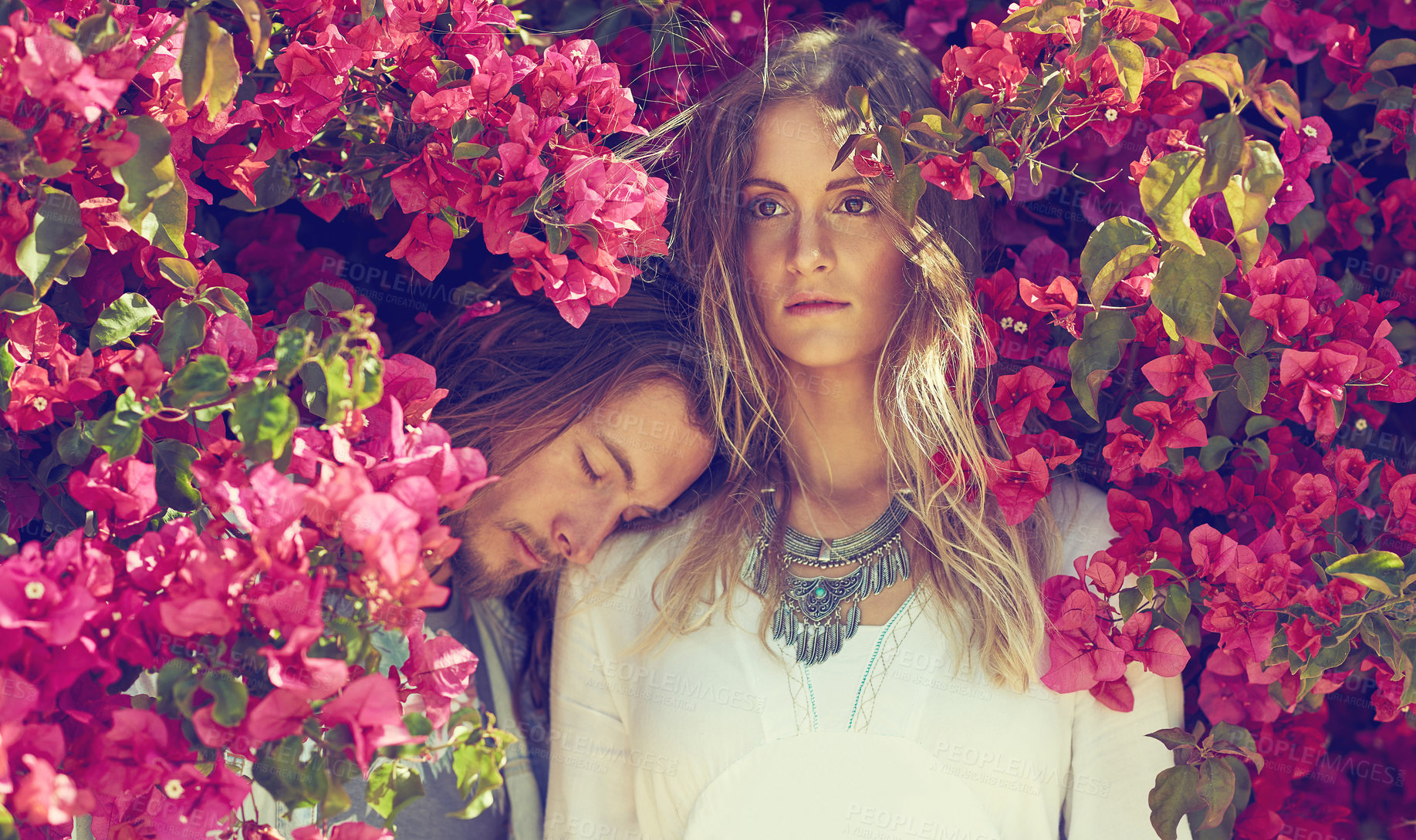 Buy stock photo Shot of a young couple standing together under a flowering bush