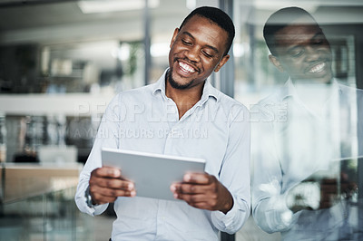 Buy stock photo Shot of a handsome young businessman standing alone in the office and using a digital tablet during the day