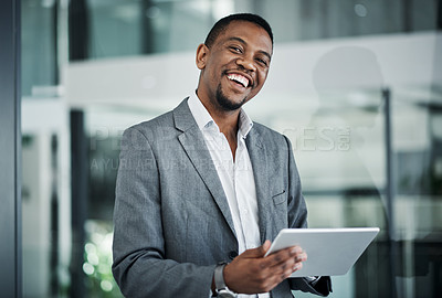 Buy stock photo Shot of a handsome young businessman standing alone in the office and using a digital tablet during the day