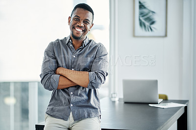 Buy stock photo Shot of a handsome young businessman standing alone in the office with his arms folded during the day