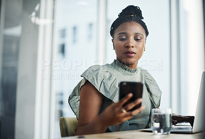 Buy stock photo Shot of an attractive young businesswoman sitting in the office and using her cellphone and laptop