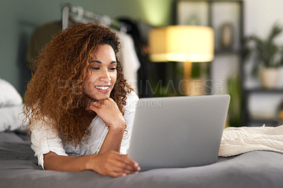 Buy stock photo Shot of a young woman using her laptop while lying on her bed