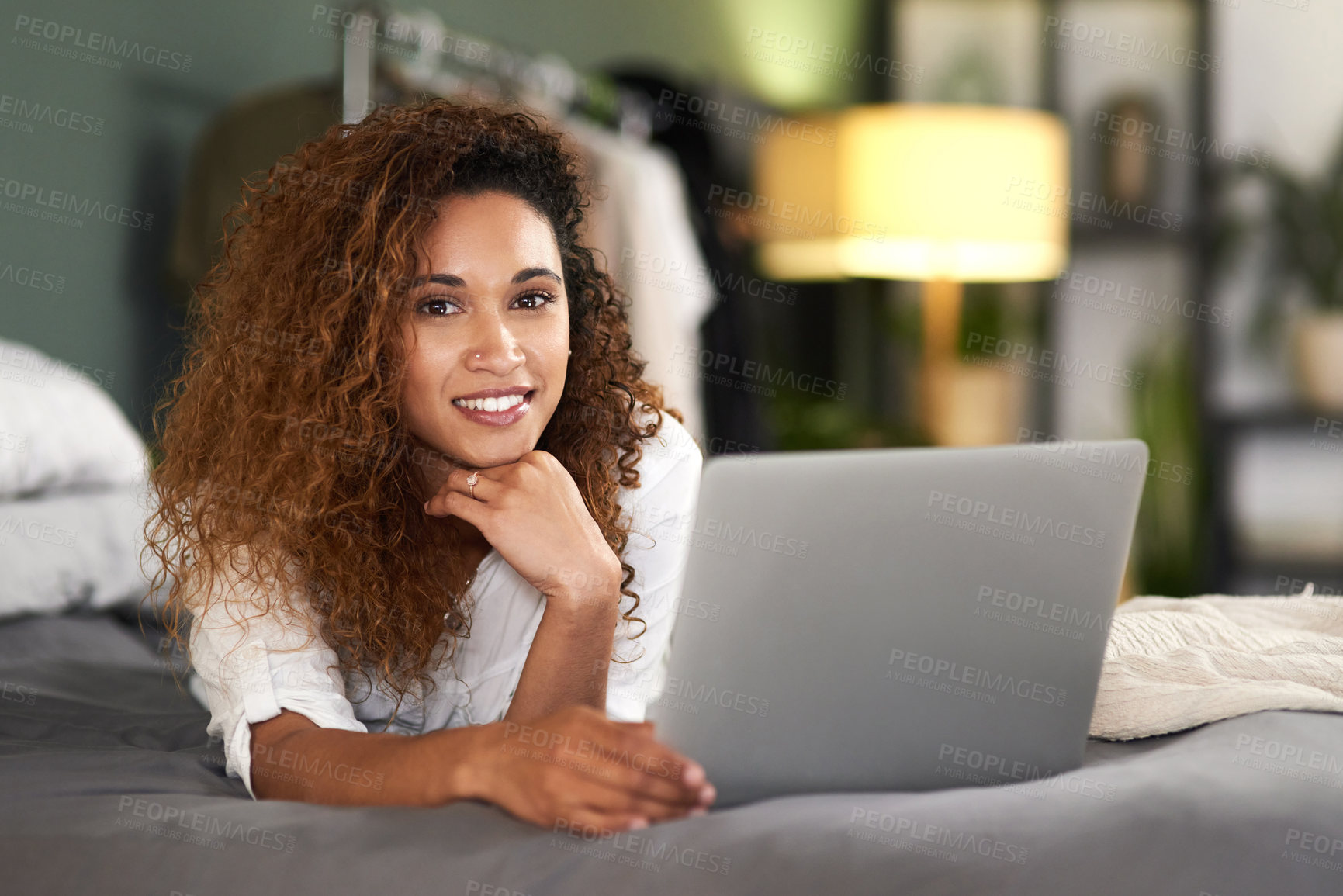 Buy stock photo Shot of a young woman using her laptop while lying on her bed