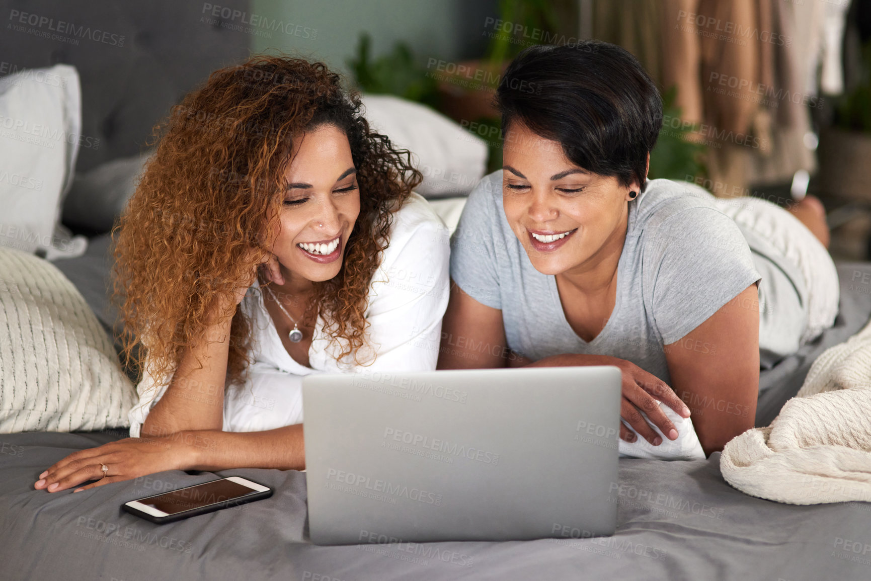 Buy stock photo Shot of a young couple using a laptop while lying on their bed