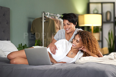 Buy stock photo Shot of a young couple using a laptop while lying on their bed