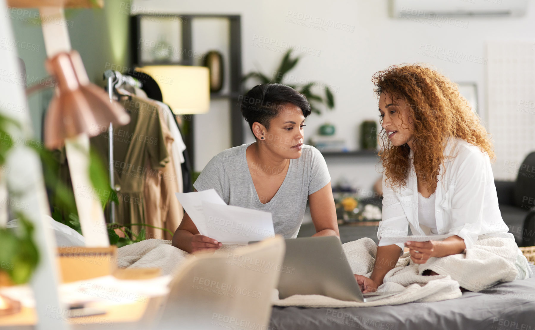 Buy stock photo Shot of a young couple holding paperwork and using a laptop while sitting at home