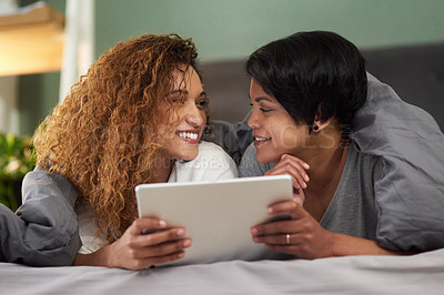 Buy stock photo Shot of a young couple using a digital tablet while lying in their bed