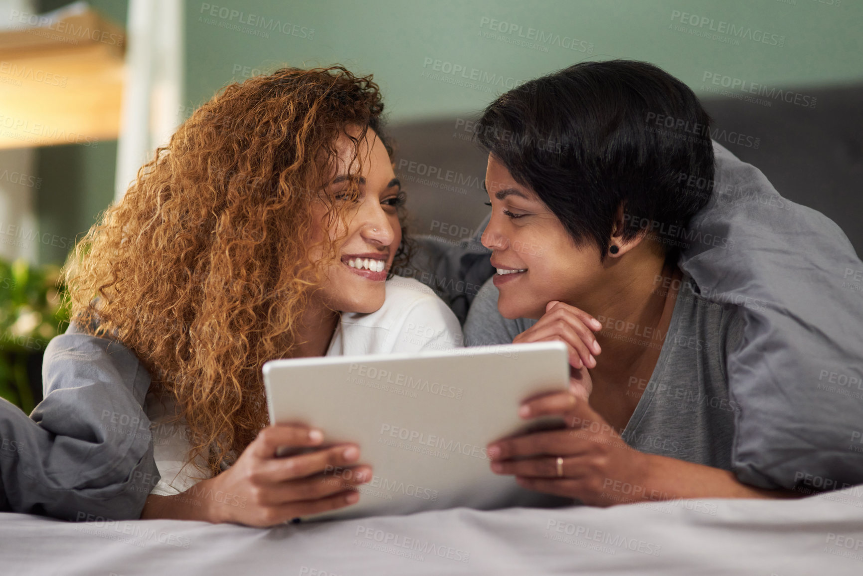 Buy stock photo Shot of a young couple using a digital tablet while lying in their bed