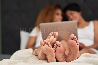 Buy stock photo Shot of a couple lying barefoot on their bed while using their laptop