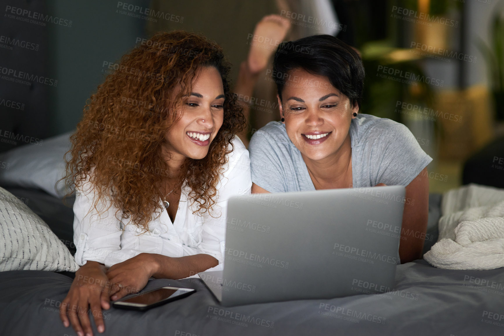 Buy stock photo Shot of a young couple using a laptop while lying on their bed