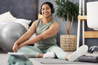 Buy stock photo Portrait of a sporty young woman stretching her legs while exercising at home