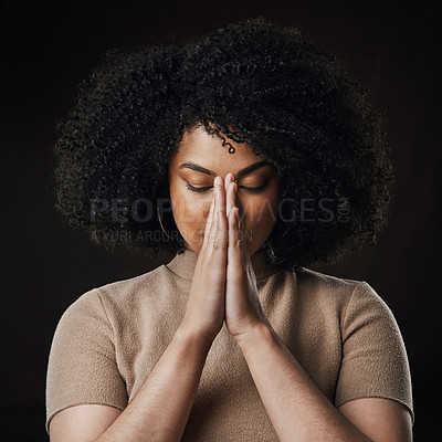 Buy stock photo Cropped shot of an attractive young woman in prayer against a dark background in studio