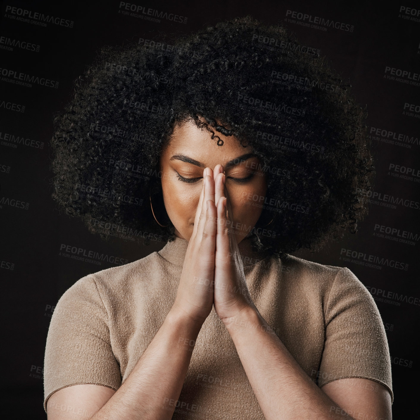 Buy stock photo Cropped shot of an attractive young woman in prayer against a dark background in studio