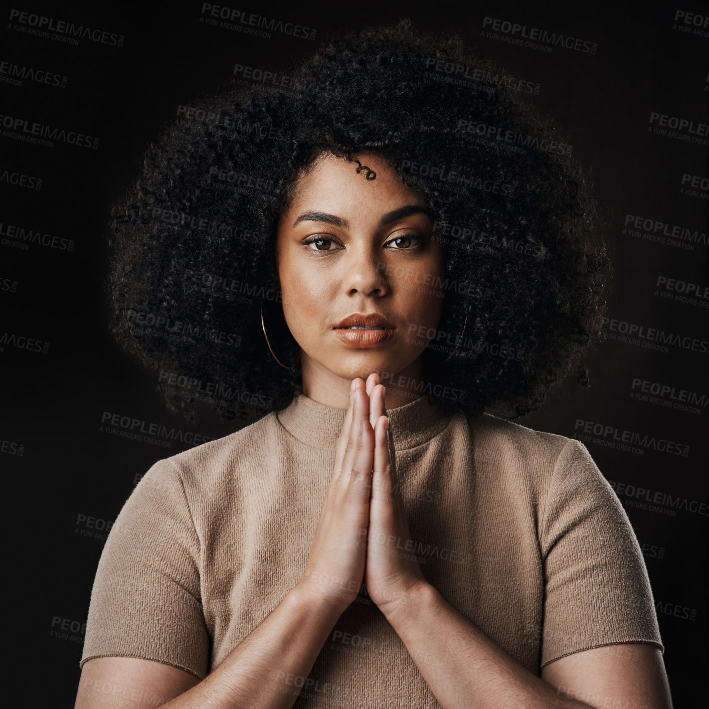 Buy stock photo Cropped portrait of an attractive young woman in prayer against a dark background in studio