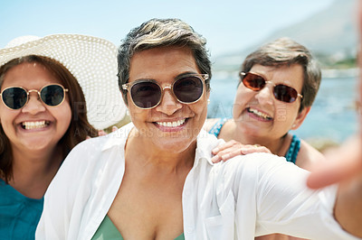 Buy stock photo Shot of a mature group of friends standing together and posing for a selfie during a day on the beach
