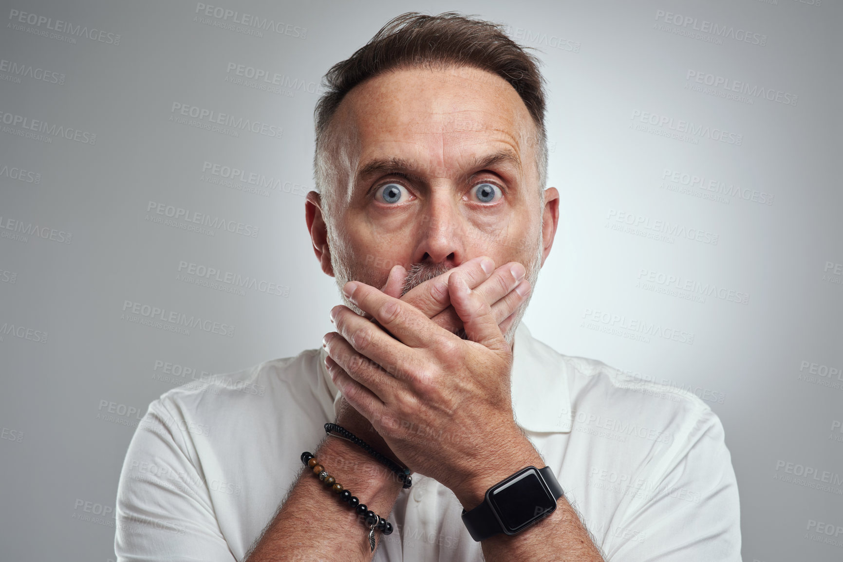 Buy stock photo Studio portrait of a mature man covering his mouth and looking shocked against a grey background