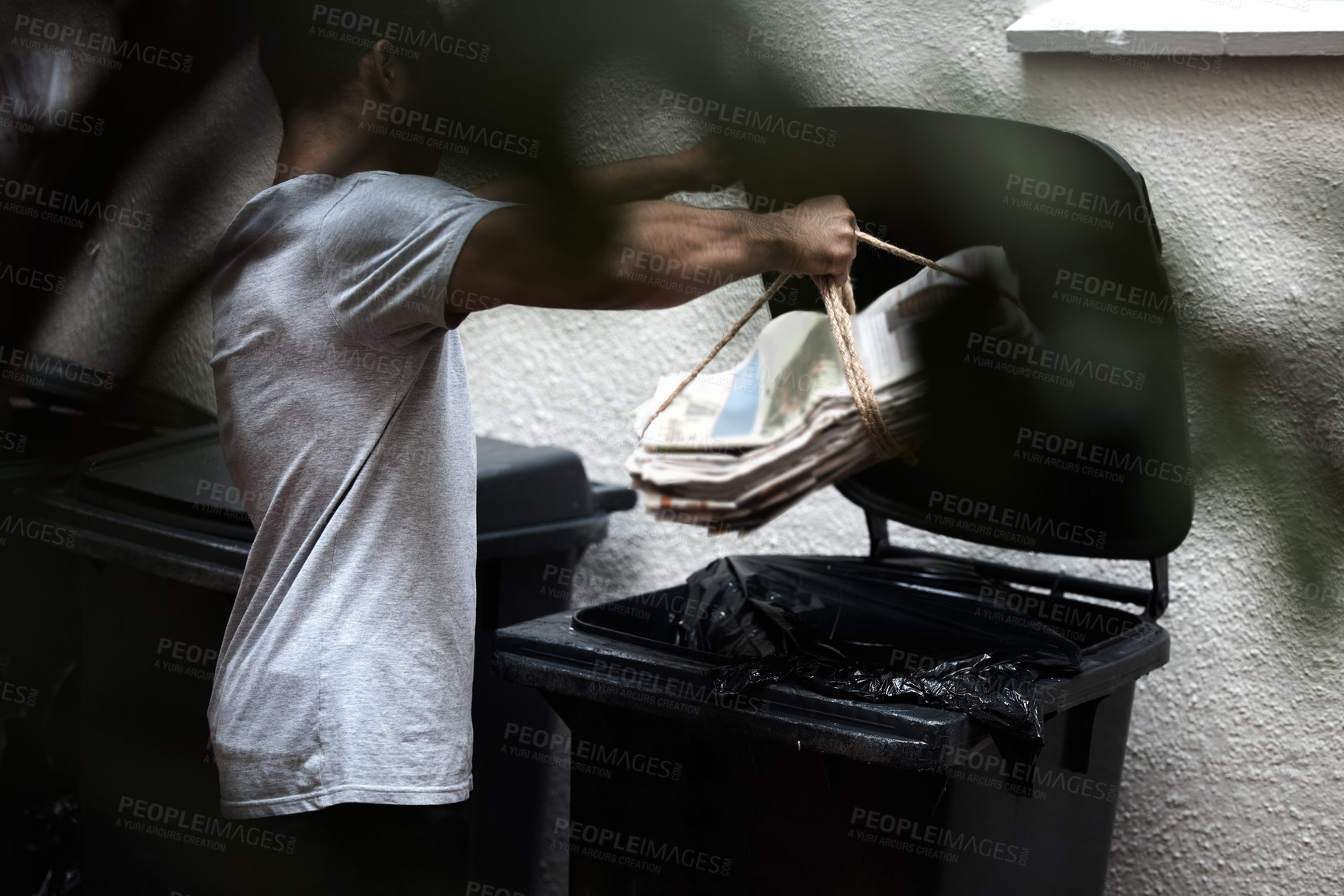 Buy stock photo Shot of a young man putting newspaper in the bin to be recycled