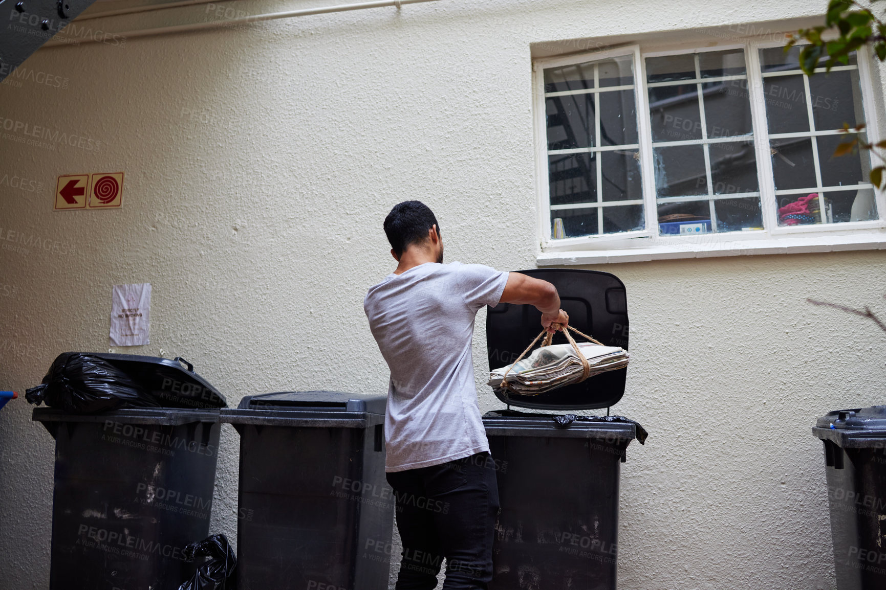 Buy stock photo Shot of a young man putting newspaper in the bin to be recycled