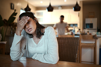Buy stock photo Shot of a woman looking stressed while sitting at home with her boyfriend standing in the background