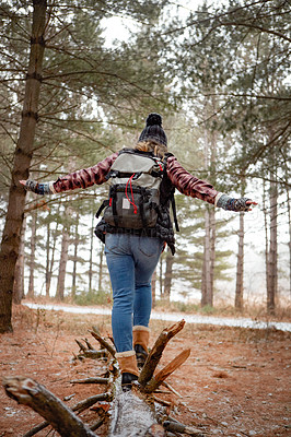 Buy stock photo Rearview shot of a young woman walking on a tree log in the wilderness during winter