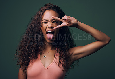 Buy stock photo Tongue out, wink and peace by gen z girl in studio with hand, sign and gesture on green background. Face, fingers and female model with crazy, personality and youth aesthetic, emoji or isolated pose