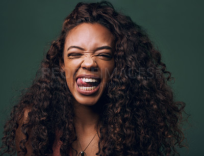 Buy stock photo Tongue out, portrait and young woman in studio with natural curly hair, happy meme or wink on a green background. Face, crazy and female model with funny personality, goofy and silly emoji expression