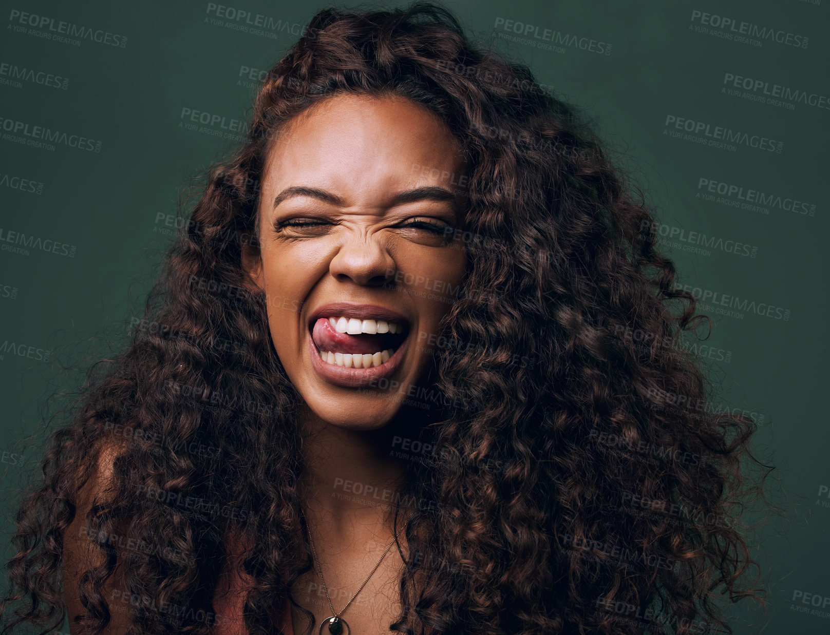 Buy stock photo Tongue out, portrait and young woman in studio with natural curly hair, happy meme or wink on a green background. Face, crazy and female model with funny personality, goofy and silly emoji expression