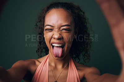 Buy stock photo Selfie, tongue out and young woman in studio with facial, expression or personality on green background. Face, emoji and crazy gen z model wink for silly profile picture, portrait or fun goofy post