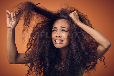 Buy stock photo Shot of a woman crying while combing our her curls against an orange background