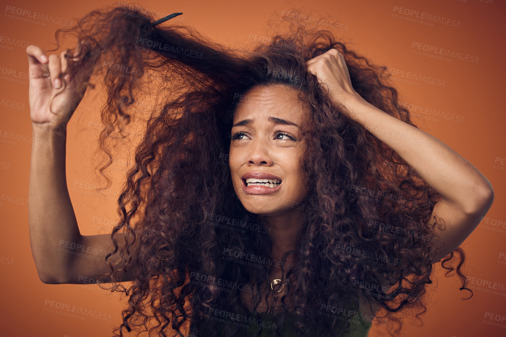 Buy stock photo Shot of a woman crying while combing our her curls against an orange background