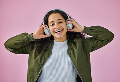 Buy stock photo Shot of an attractive young woman standing against a pink background in the studio and listening to music through headphones