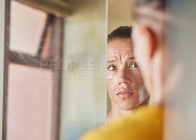 Buy stock photo Shot of a young man looking at his face in the reflection of his mirror in his bathroom at home