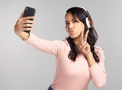 Buy stock photo Shot of a beautiful young woman wearing headphones and taking a selfie against a grey background