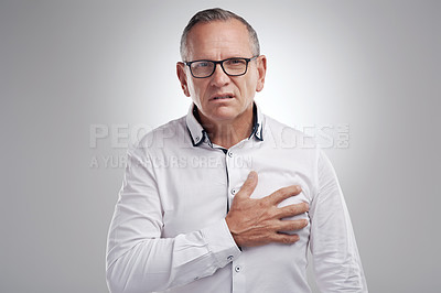 Buy stock photo Shot of a handsome mature businessman standing alone against a grey background in the studio and clutching his chest