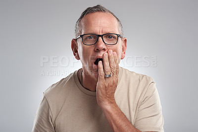 Buy stock photo Shot of a handsome mature man standing alone against a grey background in the studio and looking shocked