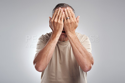 Buy stock photo Shot of a mature man standing against a grey background in the studio and covering his face with his hands
